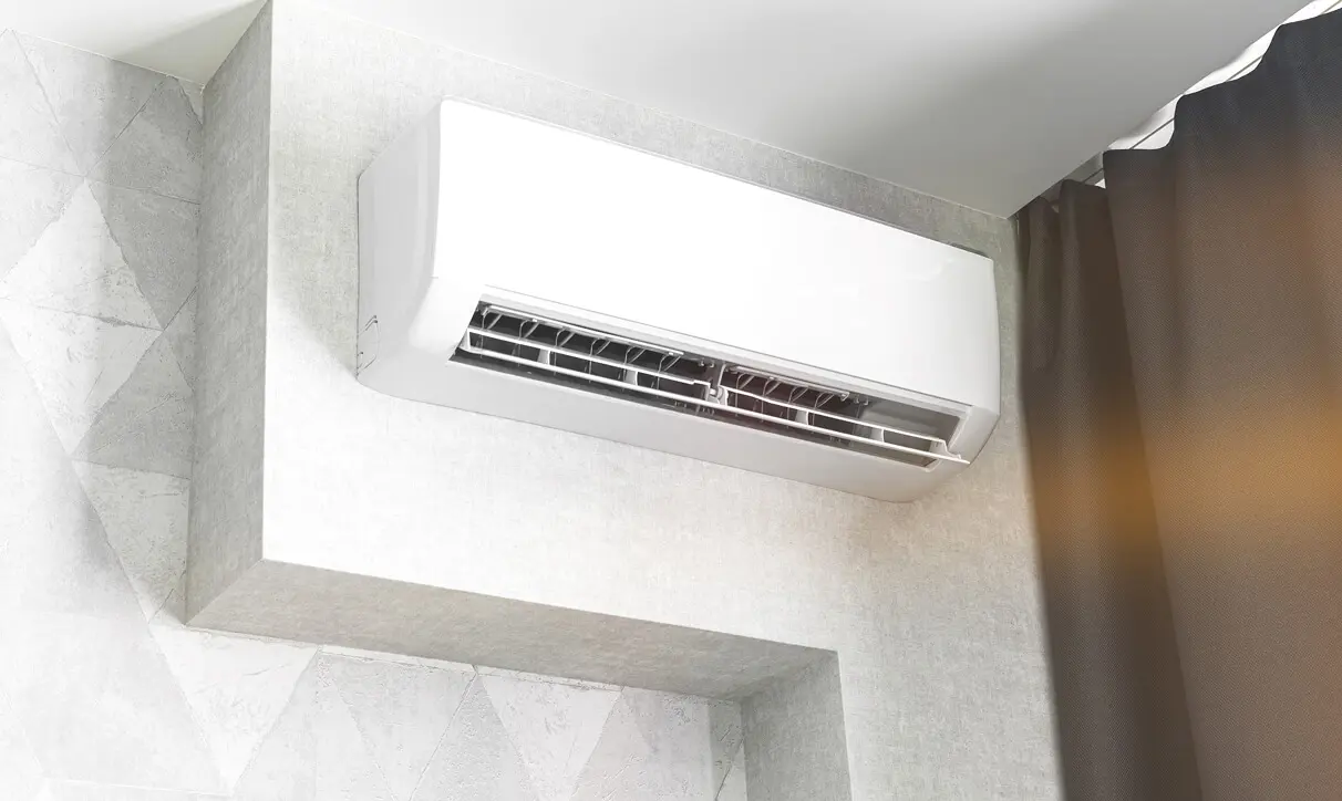 White air conditioner mounted on the wall of a bathroom, with a curtain on the right side