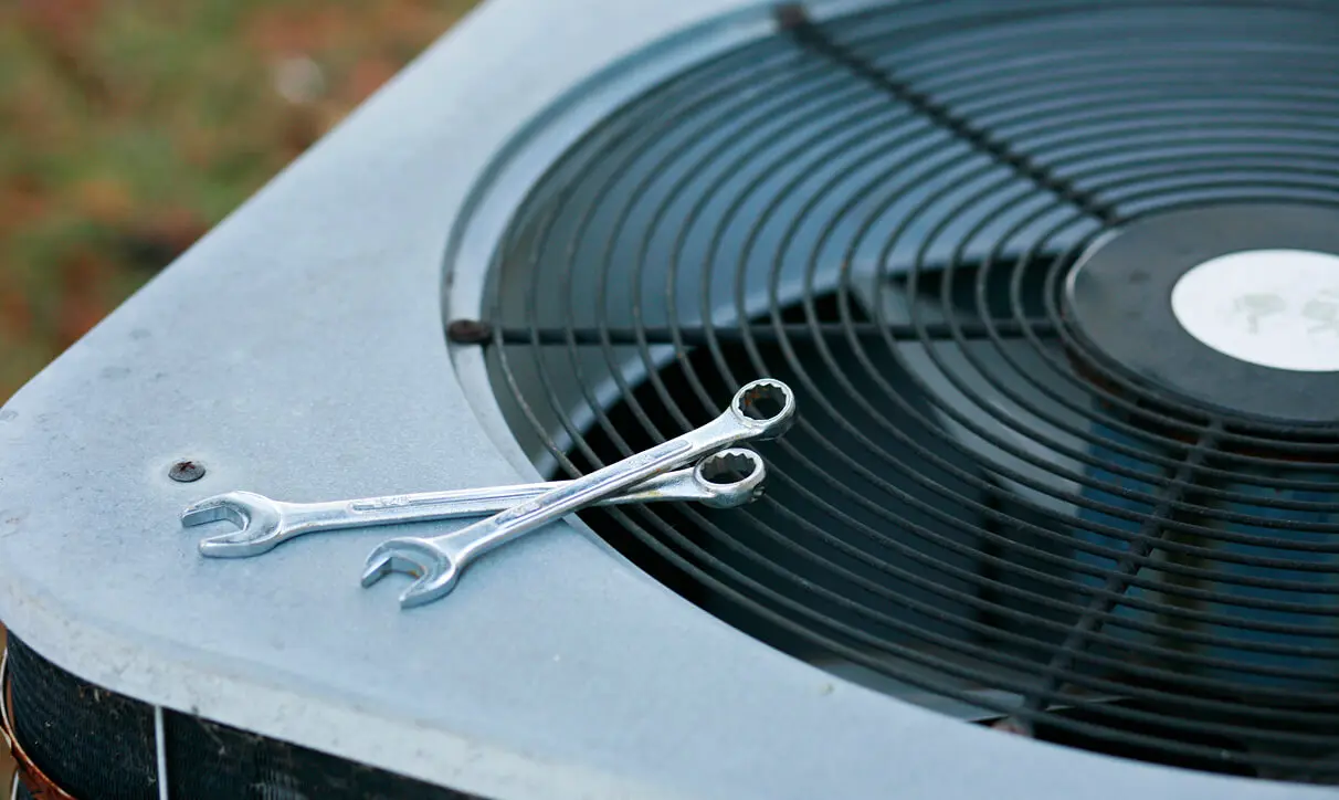 Air conditioner with two wrenches sitting on top of it, set against a blurred background