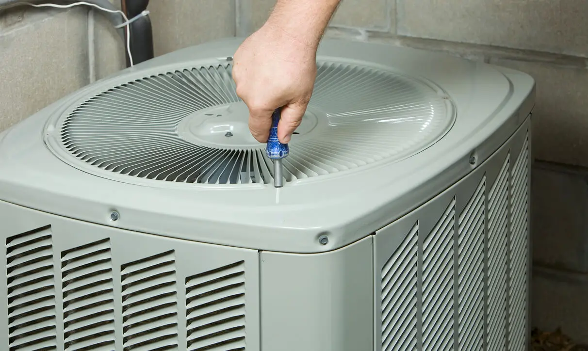 Man working on an air conditioner, holding a tool in his hand