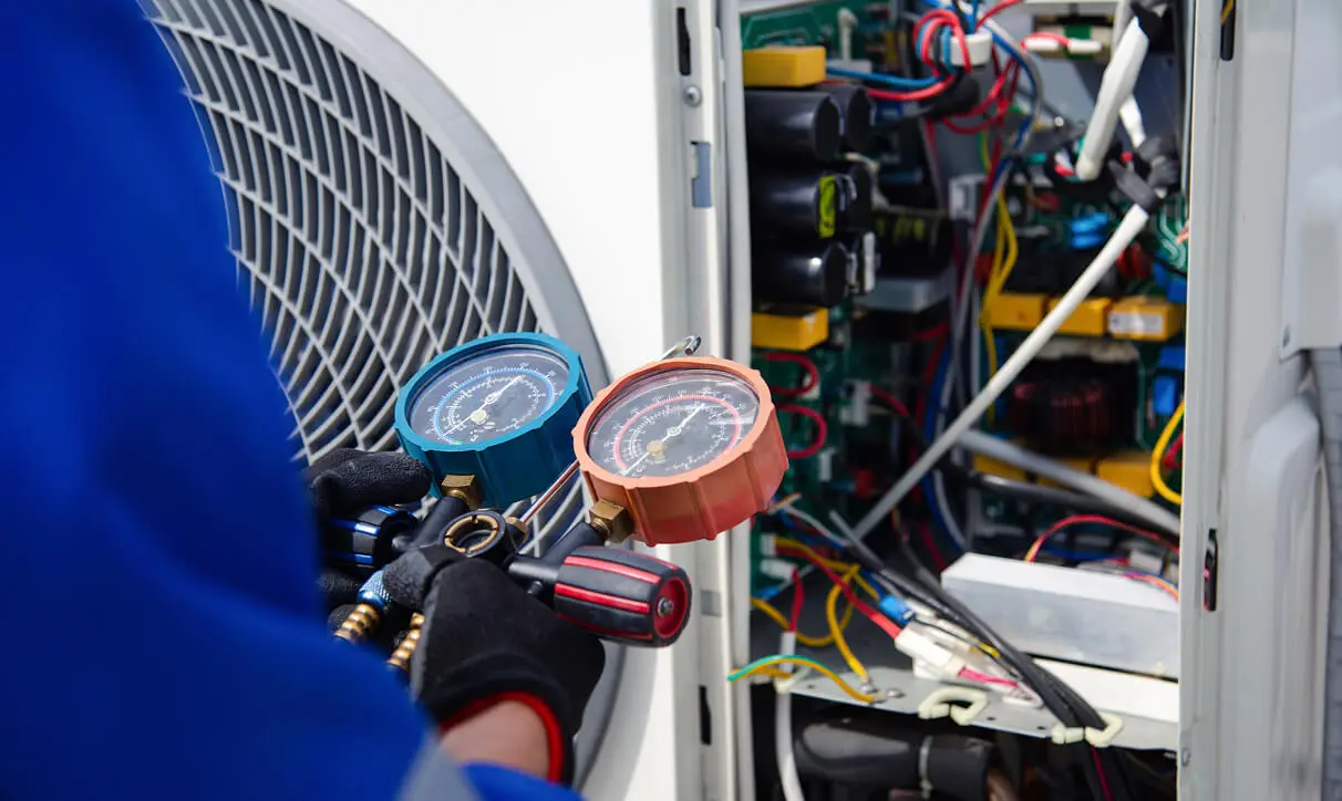 Man in a shirt holding a pressure gauge in front of an air conditioner, with a meter in his hand