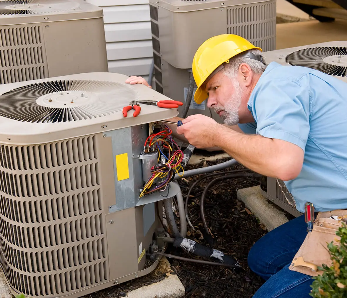 Man wearing a helmet and holding a tool while working on an air conditioner