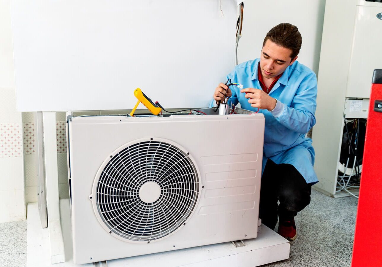 Man in a shirt and pants working on an air conditioner in a room