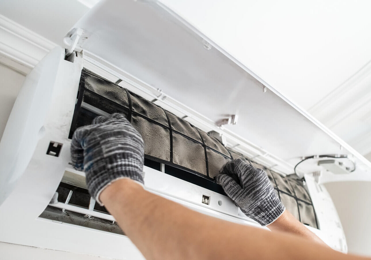 Man wearing gloves and cleaning an air conditioner in a room with a wall in the background